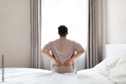 Tired man suffering from back pain after waking up