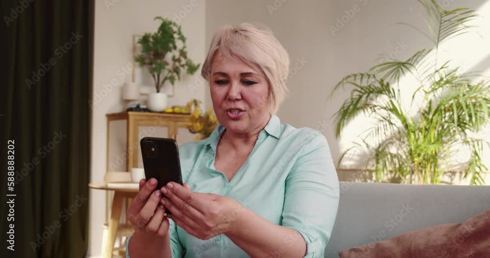 Talking to family on quarantine. Happy beautiful 50s middle aged woman using smart phone video call app at home on sofa. Talking to family on quarantine. Happy beautiful 50s middle aged woman using smart phone video call app at home on sofa.