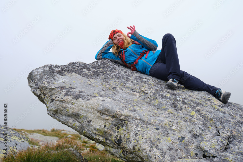 Hiking in Slovakia High Tatras mountains. Woman hiker rests on top of a large rock boulder, laying down, with fog around her.