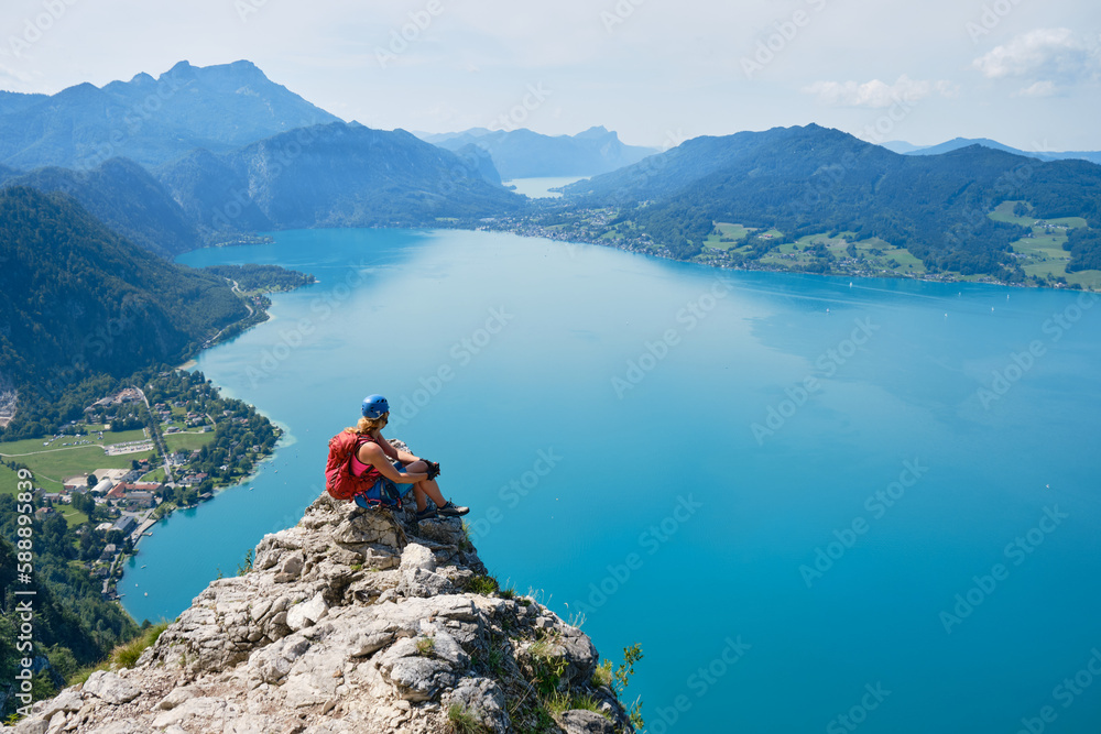 Woman above lake Attersee, Austria, at a via ferrata viewpoint, in the Summer. Courage, adventure, active, lake, activity.