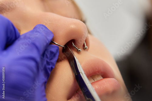 Foto Young woman doing piercing nose ring at beauty studio salon.