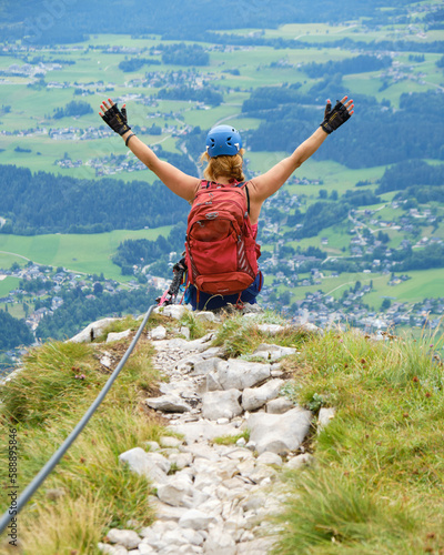 Woman on via ferrata route Sisi Loser-Panorama in Austria, spreads her arms. Summer, active, adventure, activity.