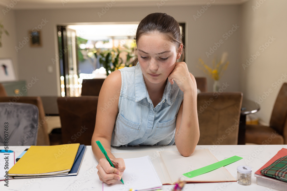 Caucasian teenager girl sitting at table and doing homework