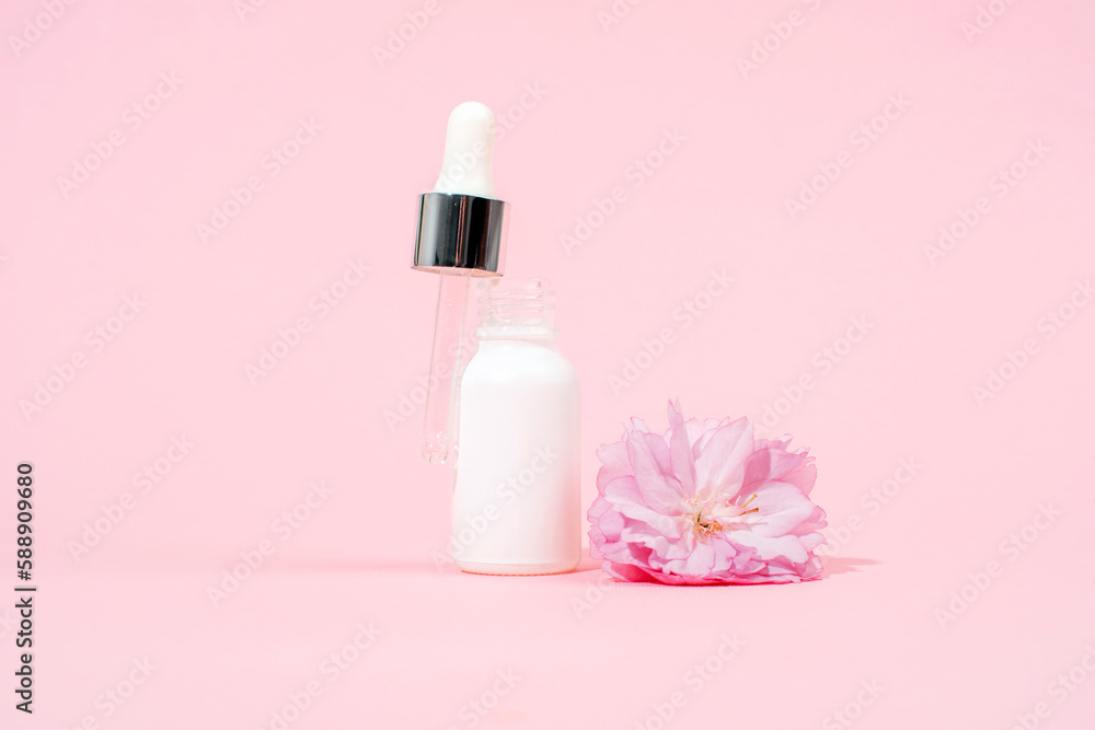 White serum dropper bottle and sakura flower on pink background. Skin care, beauty treatment concept. Mockup White serum dropper bottle and sakura flower on pink background. Skin care, beauty treatment concept. Mockup