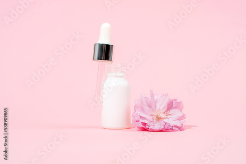 White serum dropper bottle and sakura flower on pink background. Skin care, beauty treatment concept. Mockup