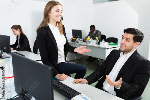 Positive young business woman flirting with man working at laptop in office photo