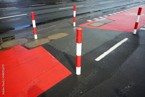 Fahrbahnmarkierung in rot und weiß auf grauem Asphalt für den Radweg mit Poller nach Regen im Sonnenschein auf der Hanauer Landstraße im Ostend von Frankfurt am Main in Hessen