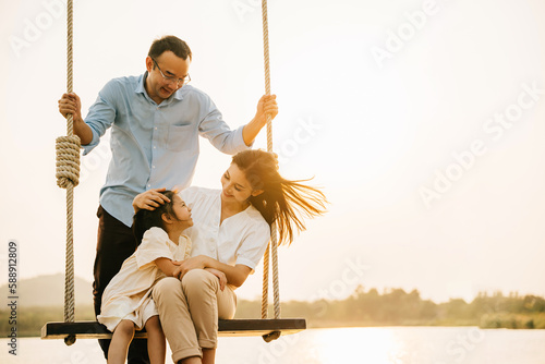 A happy family playing together on a swing set in a beautiful park, with the parents and children laughing and smiling in the sunshine, Happy Family Day