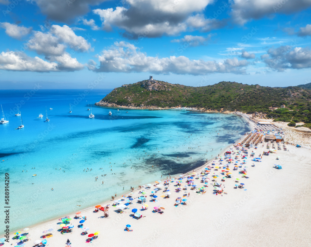 Aerial view of colorful umbrellas, white sandy beach, people, boats and yachts in blue sea, mountain, sky with clouds at summer sunny day. Tropical landscape. Travel in Sardinia, Italy. Top drone view