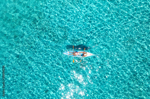 Aerial view of kayak with people in blue sea at summer sunny day. Man and woman on floating canoe in clear azure water. Sardinia island, Italy. Tropical landscape. Sup board. Active travel. Top view