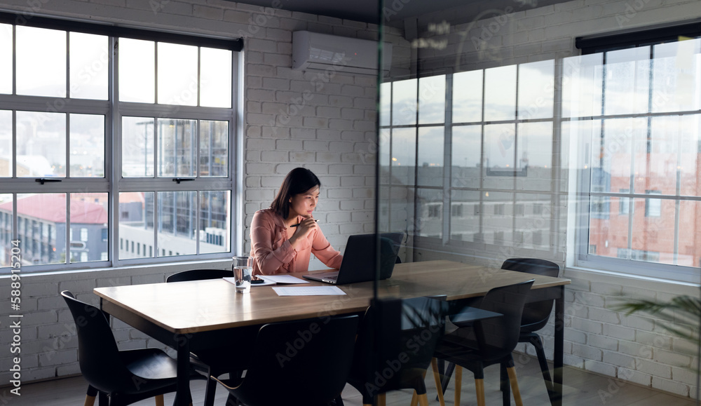 Asian businesswoman sitting at desk and using laptop, working late at office Asian businesswoman sitting at desk and using laptop, working late at office