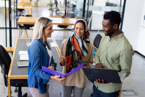 Happy diverse group of casual business people discussing work and using laptop in modern office