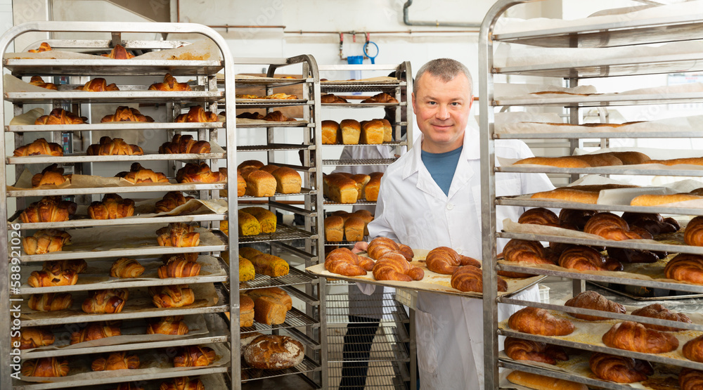 Baker putting baked bread on rack. High quality photo