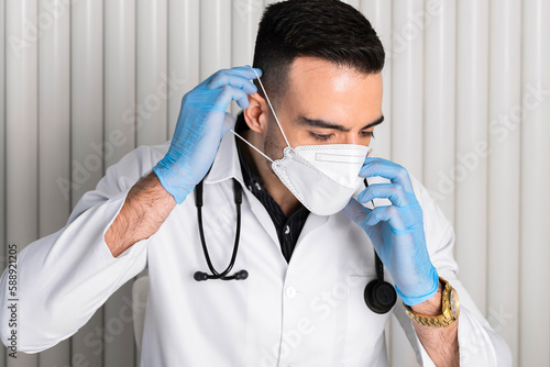 A Handsome, confident doctor in a white coat and with a stethoscope on the neck wearing a coronavirus surgical mask. face protective mask.