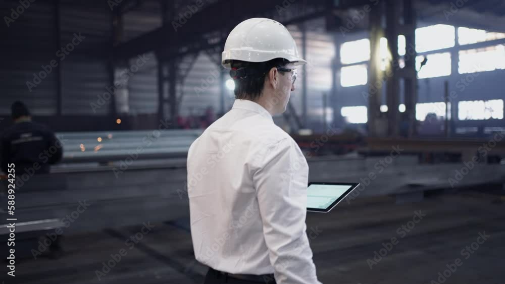 Engineer in Hard Hat is Walking Through Factory. Back View Engineer in Hard Hat is Walking Through Factory. Back View