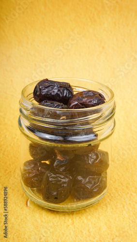 Dates fruits or Kurma in the glass jar with yellow background. Selective focus