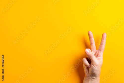 Close up of hand of caucasian woman showing peace sign with copy space on yellow background