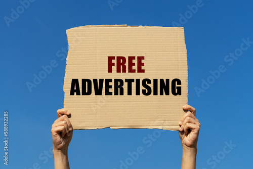 Free advertising text on box paper held by 2 hands with isolated blue sky background. This message board can be used as business concept about free advertising.