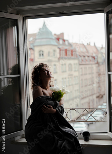 happy young woman sitting on the open window with a bouquet  © Alona