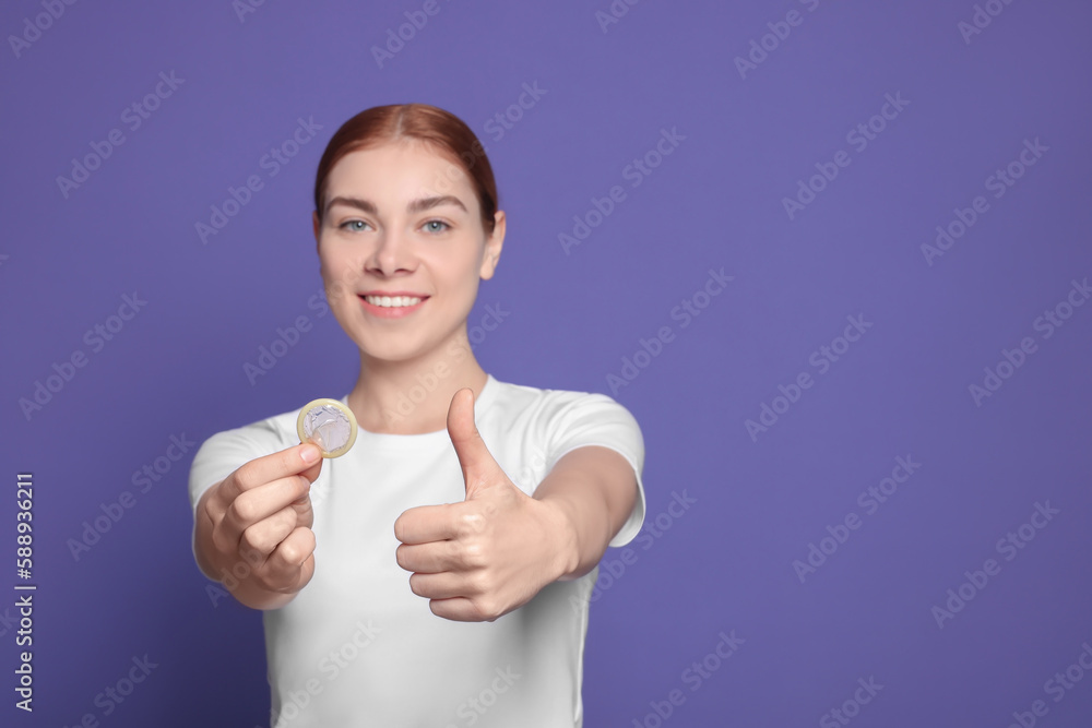 Woman with condom showing thumb up on purple background, space for text. Safe sex Woman with condom showing thumb up on purple background, space for text. Safe sex