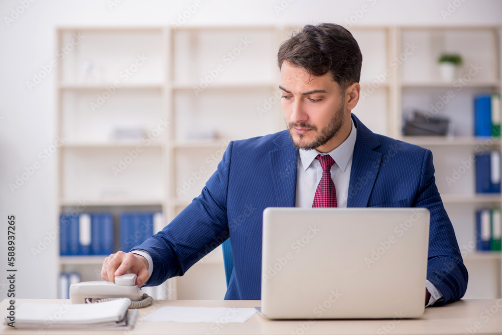 Young male employee speaking by phone at workplace Young male employee speaking by phone at workplace