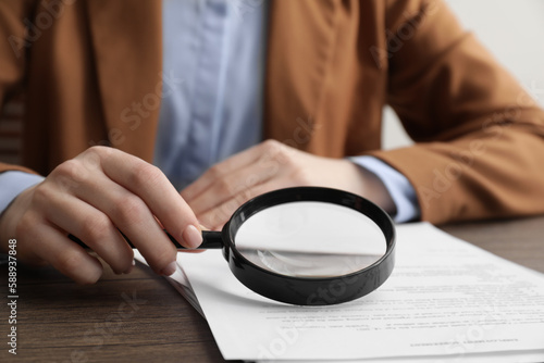 Woman looking at document through magnifier at wooden table, closeup. Searching concept
