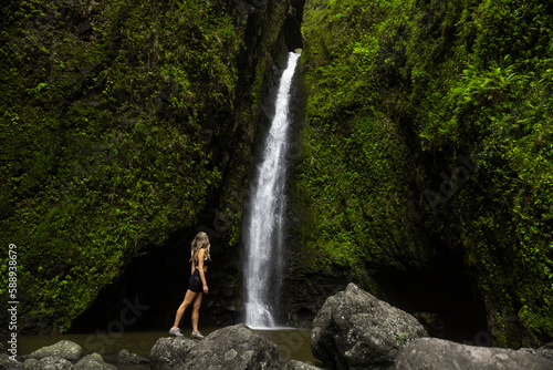 Girl hiker in front of waterfall in hawaii green jungle forest. 
