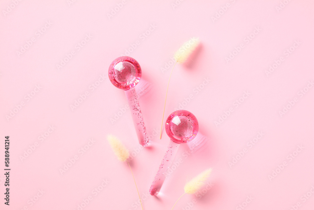 Massaging facial ice globes on pink background with dried grass