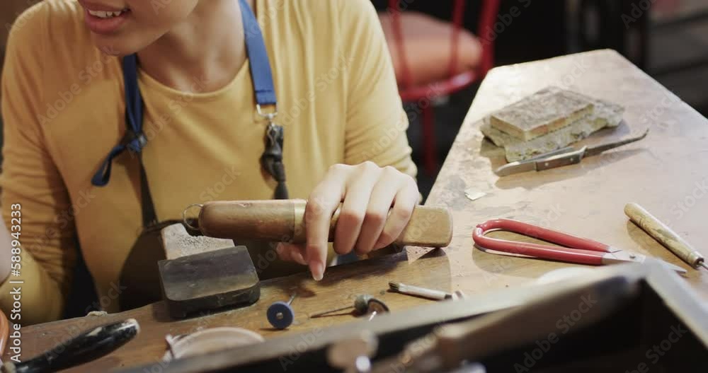 Happy biracial female worker at table shaping ring with handcraft tools in studio in slow motion Happy biracial female worker at table shaping ring with handcraft tools in studio in slow motion