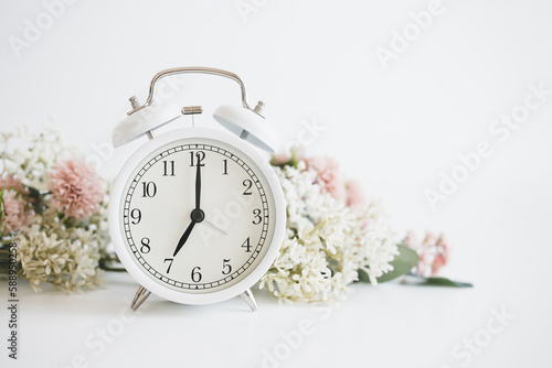 白い目覚まし時計と花　女性らしい時間のイメージ写真