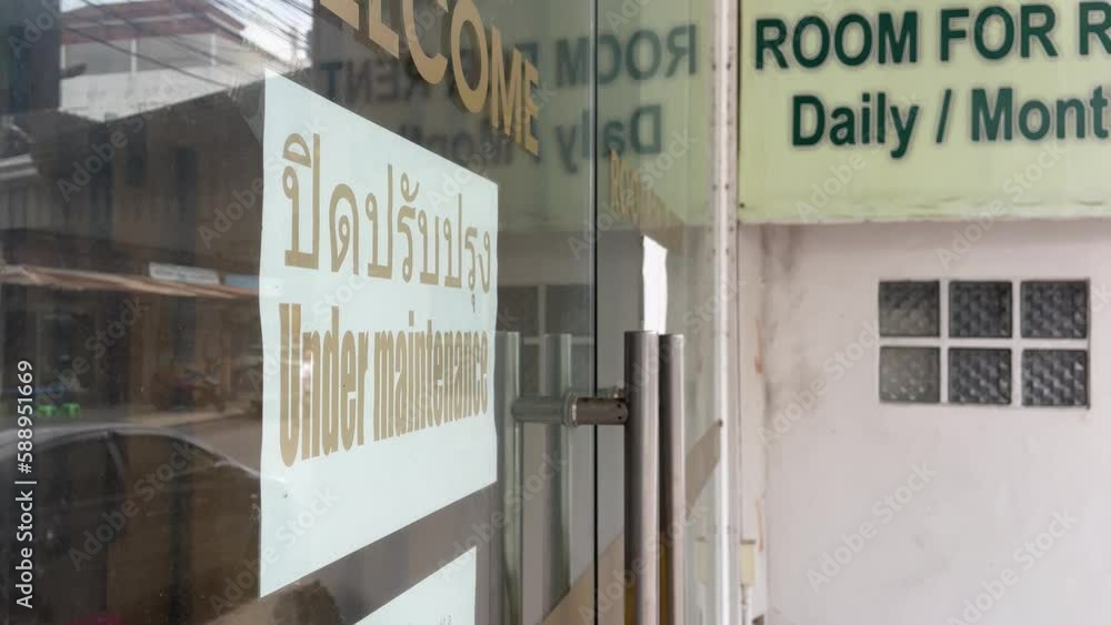 Hua Hin, Thailand - Under maintenance sign at store glass window near empty street daytime. Reflection on glass door. Closed business concept Hua Hin, Thailand - Under maintenance sign at store glass window near empty street daytime. Reflection on glass door. Closed business concept