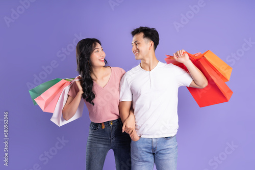 image of asian couple holding shopping bags on purple background