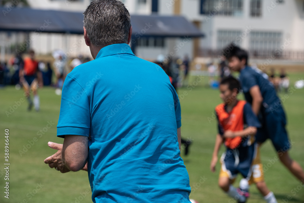 Soccer dad standing and watching his son playing football in a school tournament on a clear sky and sunny day. Sport, outdoor active, lifestyle, happy family and soccer mom soccer dad concept. Soccer dad standing and watching his son playing football in a school tournament on a clear sky and sunny day. Sport, outdoor active, lifestyle, happy family and soccer mom soccer dad concept.