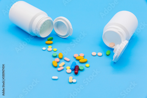 The two vials are spilled on a blue background and colorful pills and capsules are scattered on paper. There is an empty space to use as a copyspace. front view