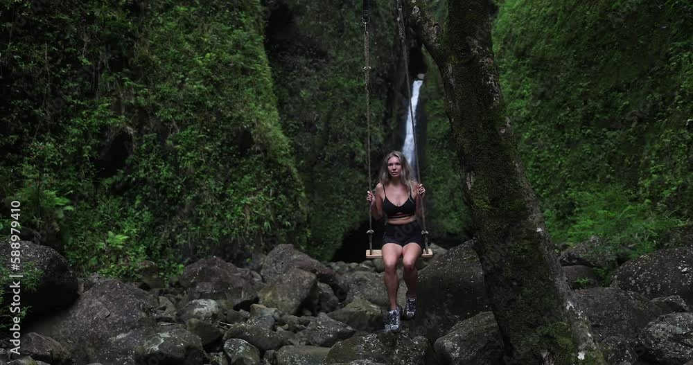 Girl hiker swings in front of a waterfall in Hawaii green jungle forest. Girl hiker swings in front of a waterfall in Hawaii green jungle forest.