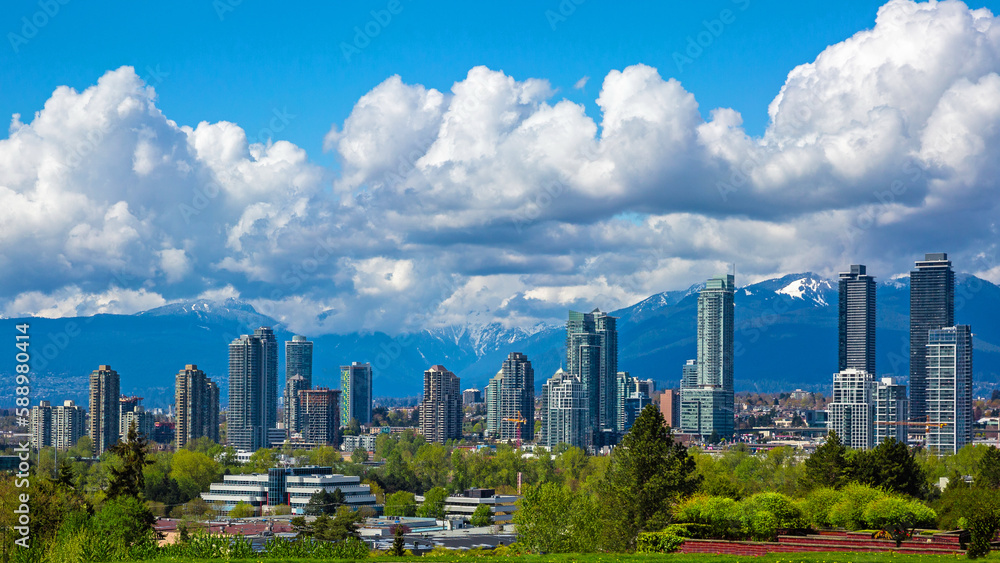 Fototapeta premium New residential area of high-rise buildings in the city of Burnaby, construction site in the center of the city against the backdrop of snow covered mountain range and blue cloudy sky