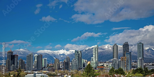 New residential area of high-rise buildings in the city of Burnaby, construction site in the center of the city against the backdrop of snow covered mountain range and blue cloudy sky