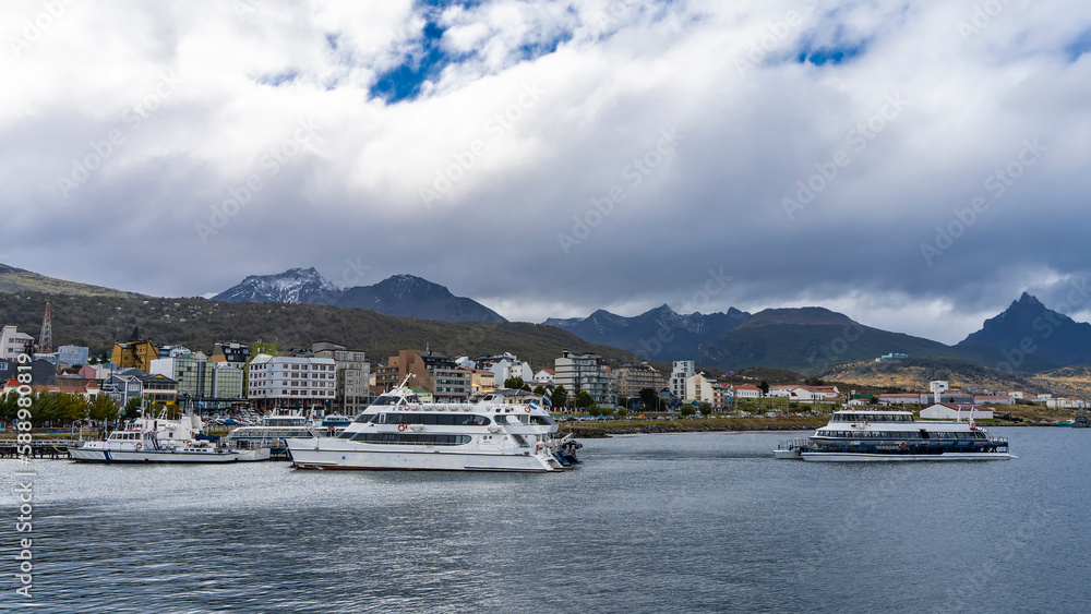 Catamarans and boats in the port of Ushuaia. There are city houses on the shore. Mountains against a background of blue sky and clouds. Argentina. Beagle Channel Catamarans and boats in the port of Ushuaia. There are city houses on the shore. Mountains against a background of blue sky and clouds. Argentina. Beagle Channel