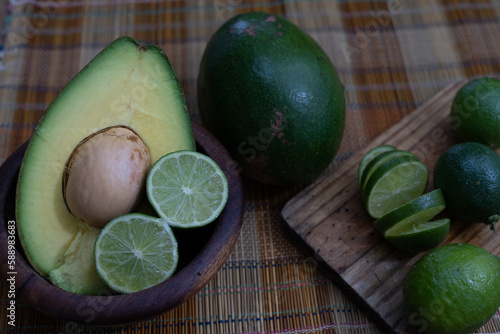 avocado on a wooden bowl, sliced limes, and whole limes on the side, wooden board