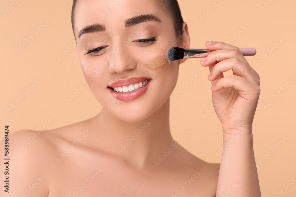 Woman applying foundation on face with brush against beige background Woman applying foundation on face with brush against beige background