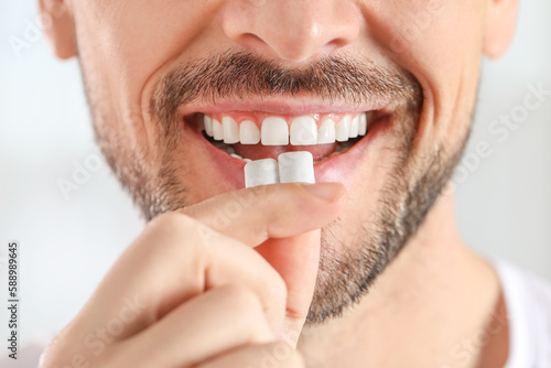 Obraz na plátně Man putting chewing gums into mouth on light background, closeup
