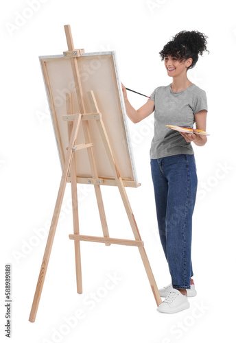 Young woman painting on easel with canvas against white background