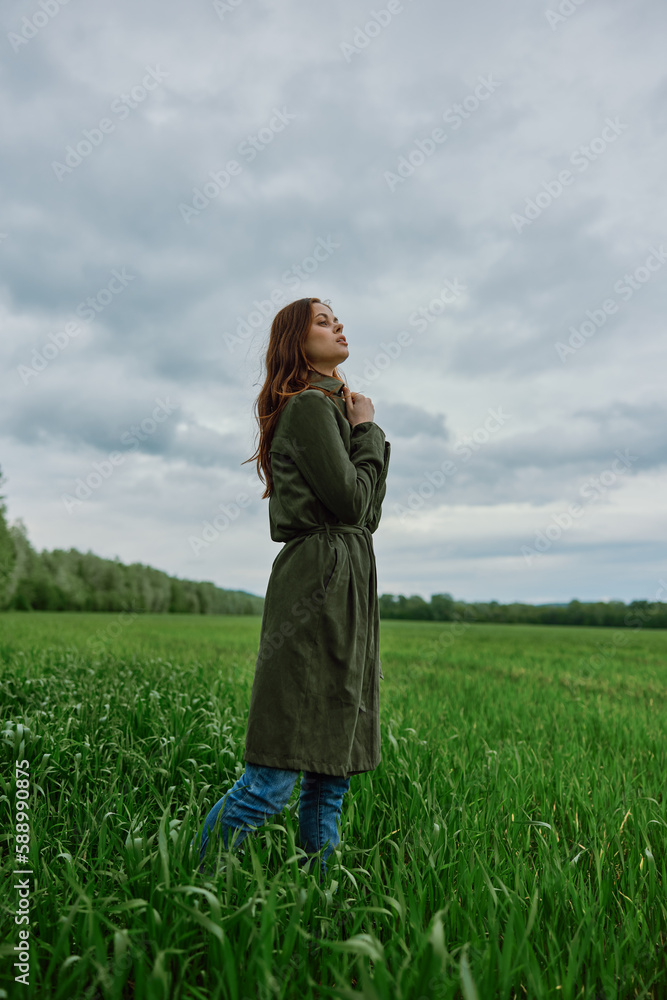Fototapeta premium a beautiful woman in a dark coat stands in a green field in the spring in rainy weather