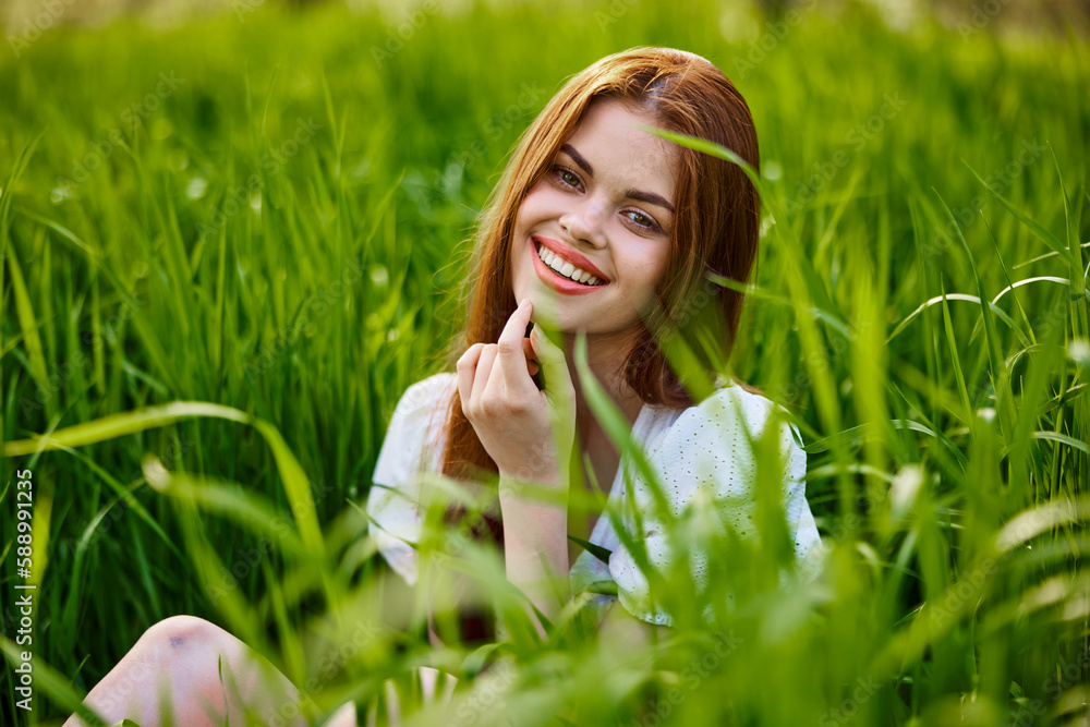 beautiful, elegant woman with red hair sits in tall green grass and smiles beautiful, elegant woman with red hair sits in tall green grass and smiles
