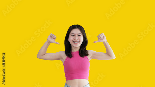 Young Asian woman pointing finger at herself, Concept of love yourself and believe in yourself, self esteem, Pointing two thumbs at herself, Isolated over yellow background.