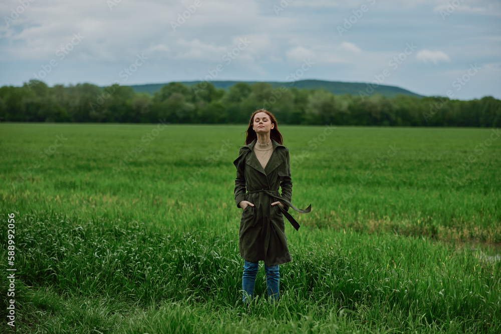 a woman stands in the middle of a green field in warm clothes. Rainy weather, walk in the forest