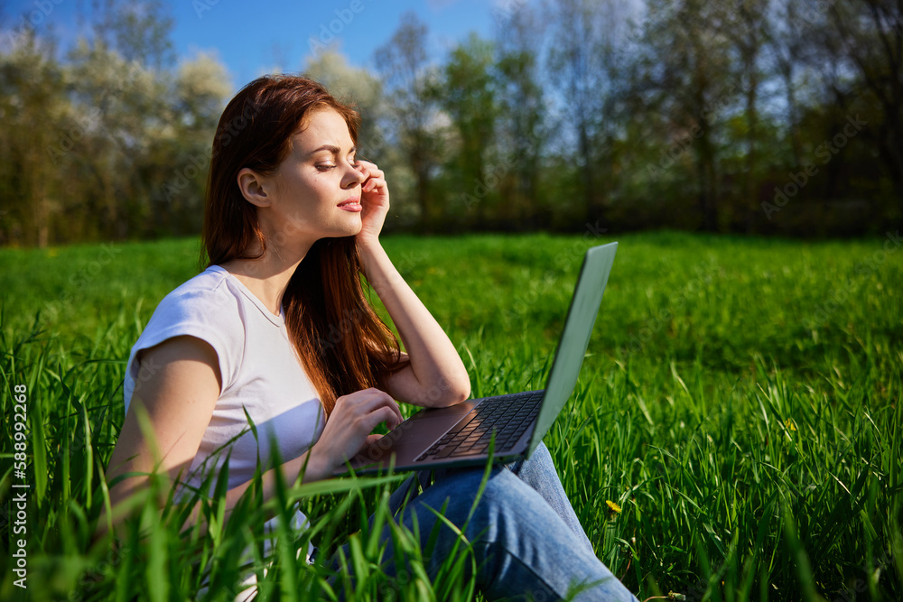 Young Caucasian woman using Laptop on nature, sitting in the grass in the park. Young Caucasian woman using Laptop on nature, sitting in the grass in the park.