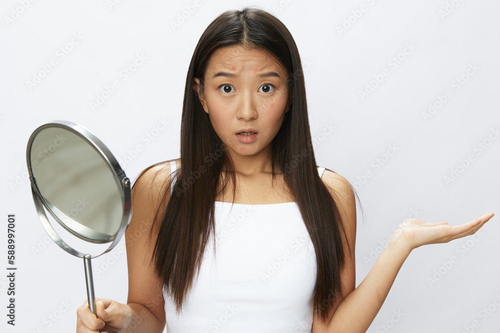 Asian woman with mirror in hand facial skin problems, acne and inflammation, red rash and allergies, chicken pox, sadness from rashes. Facial skin care concept for diseases and nerves Asian woman with mirror in hand facial skin problems, acne and inflammation, red rash and allergies, chicken pox, sadness from rashes. Facial skin care concept for diseases and nerves
