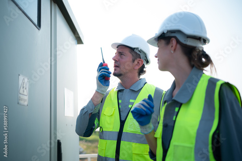 A team of electrical engineers is inspecting an energy storage station of a solar panels in the middle of a hundred acre field of solar panels. photo