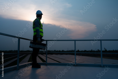 Electrical engineers inspecting solar panels in a hundred acres of grass on the rooftop of energy storage station, in the evening after completing the daily work tasks with the setting sun.